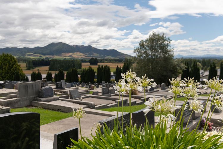 Scenic view of Gore Cemetery with white flowers in the foreground, gravestones, and a backdrop of rolling hills and a partly cloudy sky